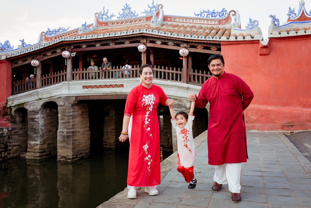 A family wearing red ao dai in front of the Japanese Covered Bridge in Hội An, Vietnam.